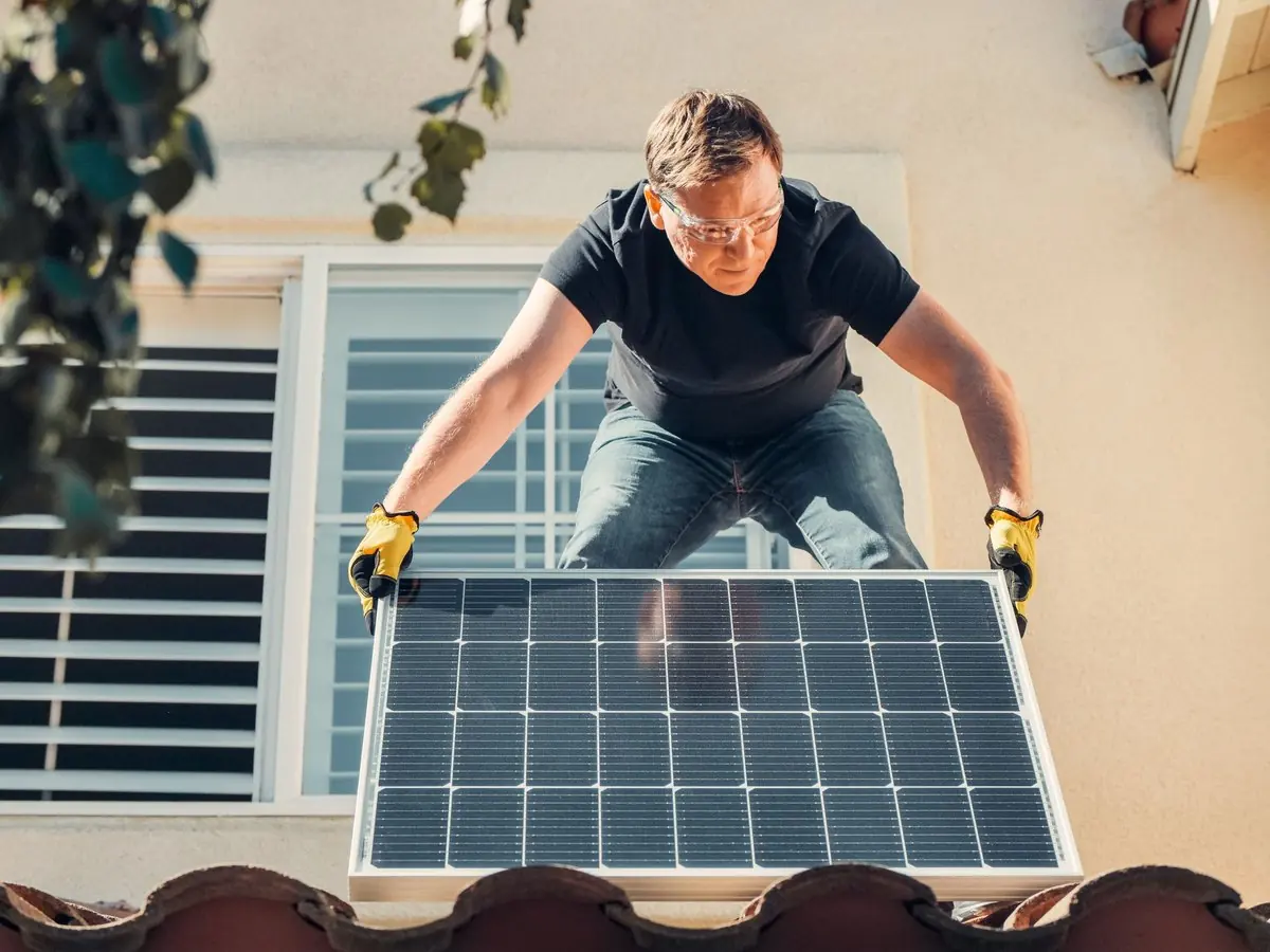 Instalador subiendo un panel solar al techo de una casa